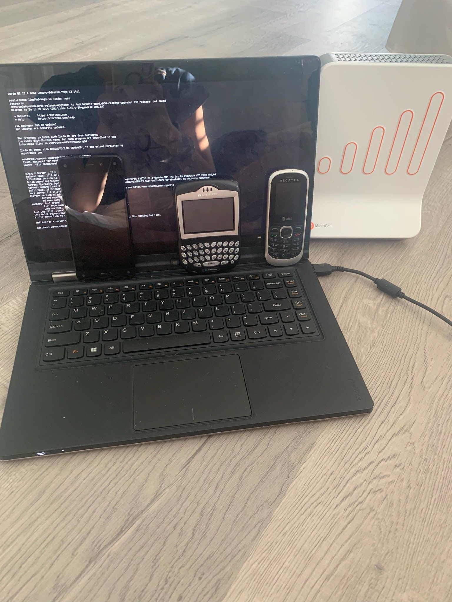 RCM test setup: a Linux laptop terminal with a BlackBerry and an Alcatel handset propped against the screen, beside a cellular MicroCell base station.
